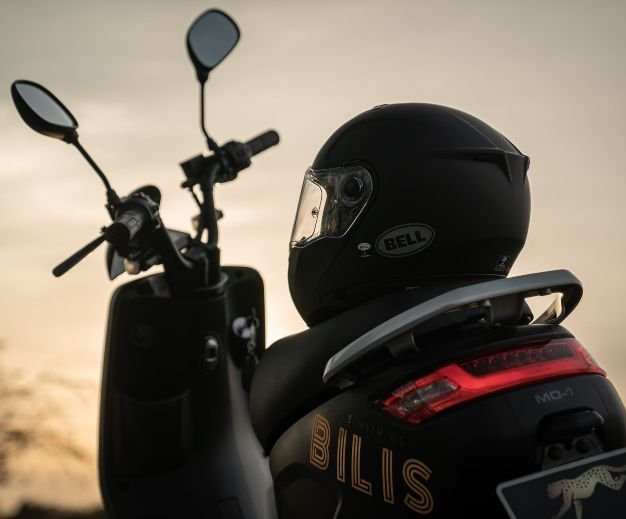 a Bell helmet on top of the seat of a Bilis electric moped. sunset.