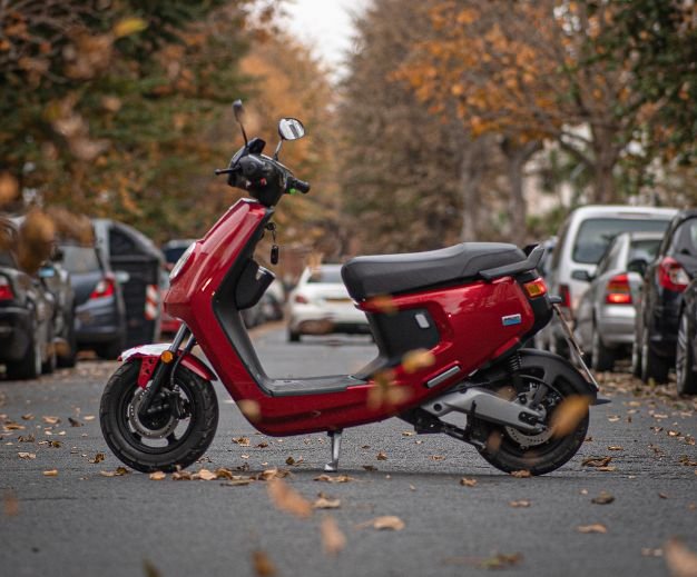 niu MQi plus sport in red on a road with blowing leaves.