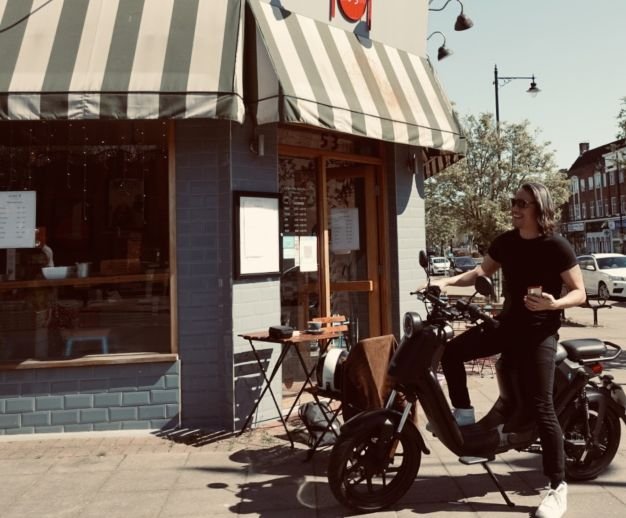 man outside a coffe shop on his black electric moped