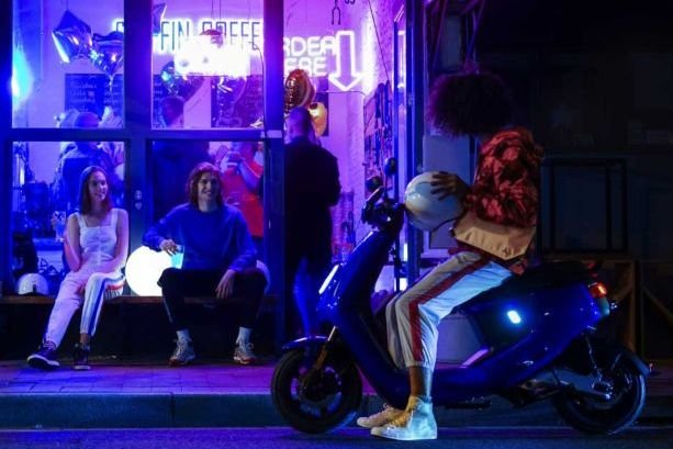 young man on an electric moped outside a coffee shop at night